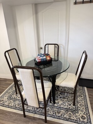 A dining area with a glass table, four chairs, a rug, and a door in the background. - 🏡 Modern 2-Bedroom Private Suite Near Niagara Falls | Sleeps 4 | Free Parking (Thorold)