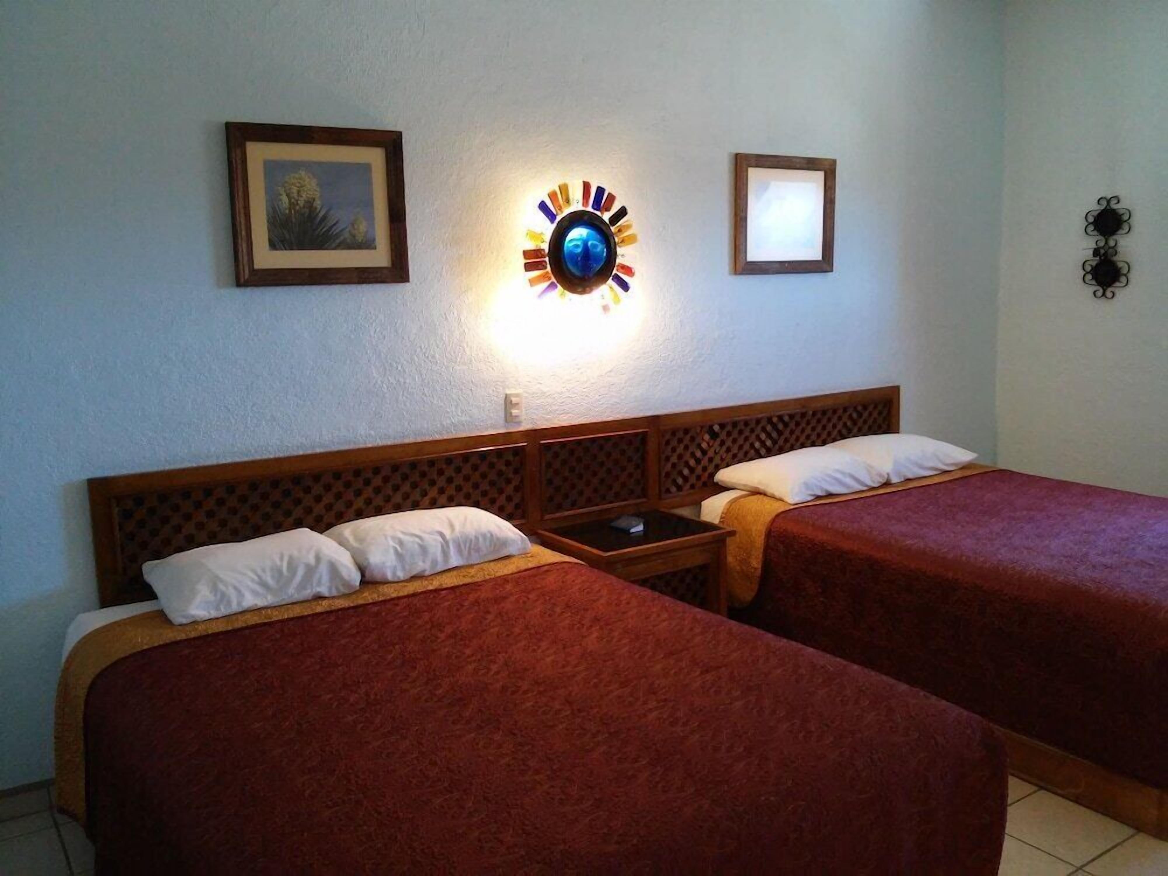 A hotel room with two beds, a nightstand, a wall clock, and framed pictures.. Hotel Mision Santa Ma Catavina