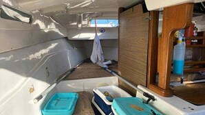 Interior de un barco con un mueble de madera, dos contenedores azules y una toalla blanca colgada.