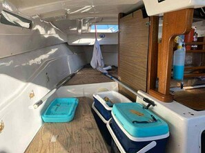 Interior de un barco con un mueble de madera, dos contenedores azules y una toalla blanca colgada.