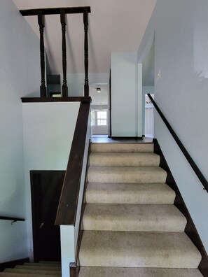 A staircase with a wooden handrail and carpeted steps leading to a landing. - Marvelous 3-room townhome in Raytown. 5-8 min from stadiums, World Cup! (Raytown)