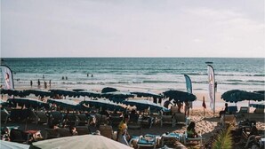 Ein Strand mit Reihen von Sonnenschirmen und Liegestühlen, ein sandiger Uferstreifen und das Meer im Hintergrund.