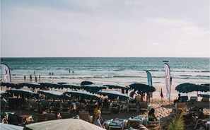 Une plage bordée de rangées de parasols et de chaises longues, un rivage sablonneux et l’océan en toile de fond.
