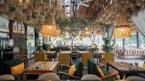 An indoor dining area with wooden tables and chairs, hanging rattan lamps, and large windows. - Sugar Marina Hotel Pop, Kata Beach (Karon)