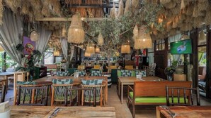 Ein Restaurant mit Holztischen, hängenden Rattanlampen und einem Fernsehbildschirm.