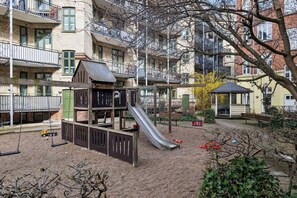 Ein Spielplatz mit Rutsche und Schaukeln, umgeben von mehrstöckigen Gebäuden.