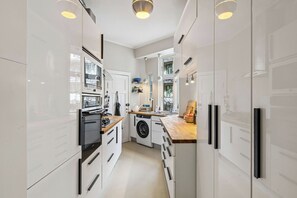 Eine moderne Küche mit weißen Schränken, einem Einbauofen, einer Waschmaschine und einer Holz Arbeitsplatte.