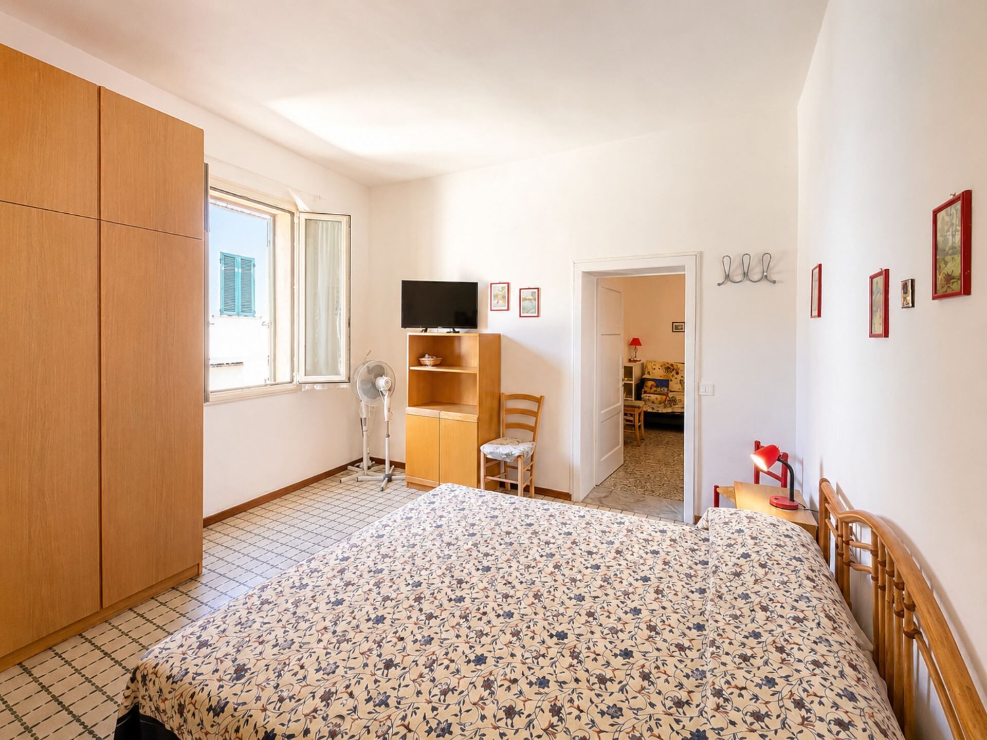 Ein Schlafzimmer mit Bett, Kleiderschrank, Fernseher, Ventilator und einer Tür zu einem anderen Raum.