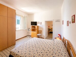 A bedroom with a bed, a wardrobe, a TV, a fan, and a door leading to another room. - Casa di Nonna Albina (Cavo)