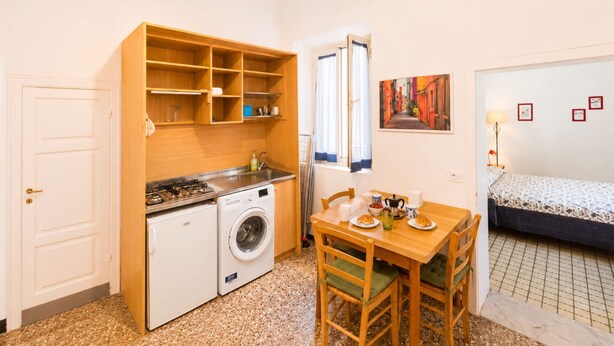 Una cocina compacta con lavadora, una mesa de comedor con sillas, una cama y un cuadro en la pared.