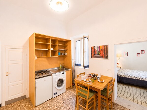 A compact kitchen with a washing machine, a dining table with chairs, a bed, and a painting on the wall. - Casa di Nonna Albina (Cavo)