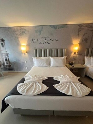 Habitación de hotel con una cama, dos mesitas de noche, una lámpara de pared y un mural.