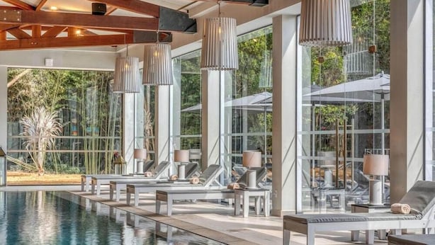 A poolside area with lounge chairs, a pool, and large windows offering views of greenery. - Vila Gale Collection Ouro Preto (Ouro Preto)