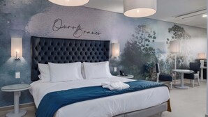 A modern hotel room with a large bed, a mural on the wall, and a seating area with tables and chairs. - Vila Gale Collection Ouro Preto (Ouro Preto)