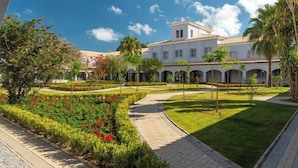 A courtyard with a pathway, a building with arches, and a garden with red flowers. - Vila Gale Collection Ouro Preto (Ouro Preto)