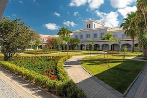 A courtyard with a pathway, a building with arches, and a garden with red flowers. - Vila Gale Collection Ouro Preto (Ouro Preto)