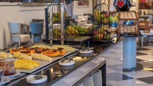 A buffet with various food items, including fruits and pastries, arranged on a counter with a checkered floor. - Vila Gale Collection Ouro Preto (Ouro Preto)