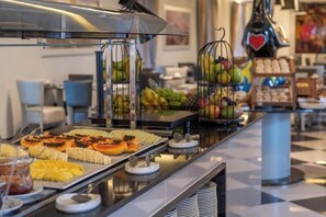 Un bufé con diversos alimentos, incluyendo frutas y pastelería, dispuesto sobre un mostrador con piso a cuadros.
