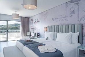 A hotel room with a large bed, a bedside table, a chair, a window with a view, and a wall with a mural. - Vila Gale Collection Ouro Preto (Ouro Preto)