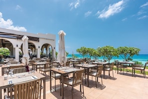 An outdoor dining area with tables and chairs, umbrellas, and a view of the ocean. - Hotel Riu Palace Swahili - Adults Only - All Inclusive (Nungwi)