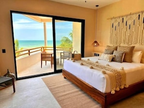 A bedroom with a large bed, a sliding glass door leading to a balcony with a view of the ocean, and a macrame wall hanging. - Ana y Jose Hotel Beach Club Holbox (Isla Holbox)
