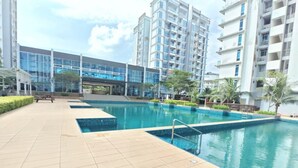 Una piscina con suelo de baldosas, rodeada de follaje y edificios modernos.