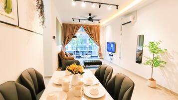 A dining area with a long table set for four, a sofa in the background, and a television on the wall.