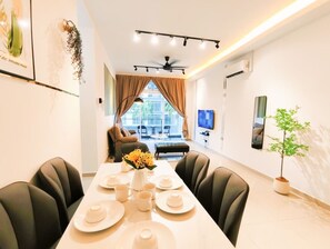 A dining area with a long table set for four, a sofa in the background, and a television on the wall. - Senai Apartment (Senai)