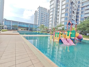 Una piscina con zona de juegos para niños, rodeada de edificios residenciales altos.