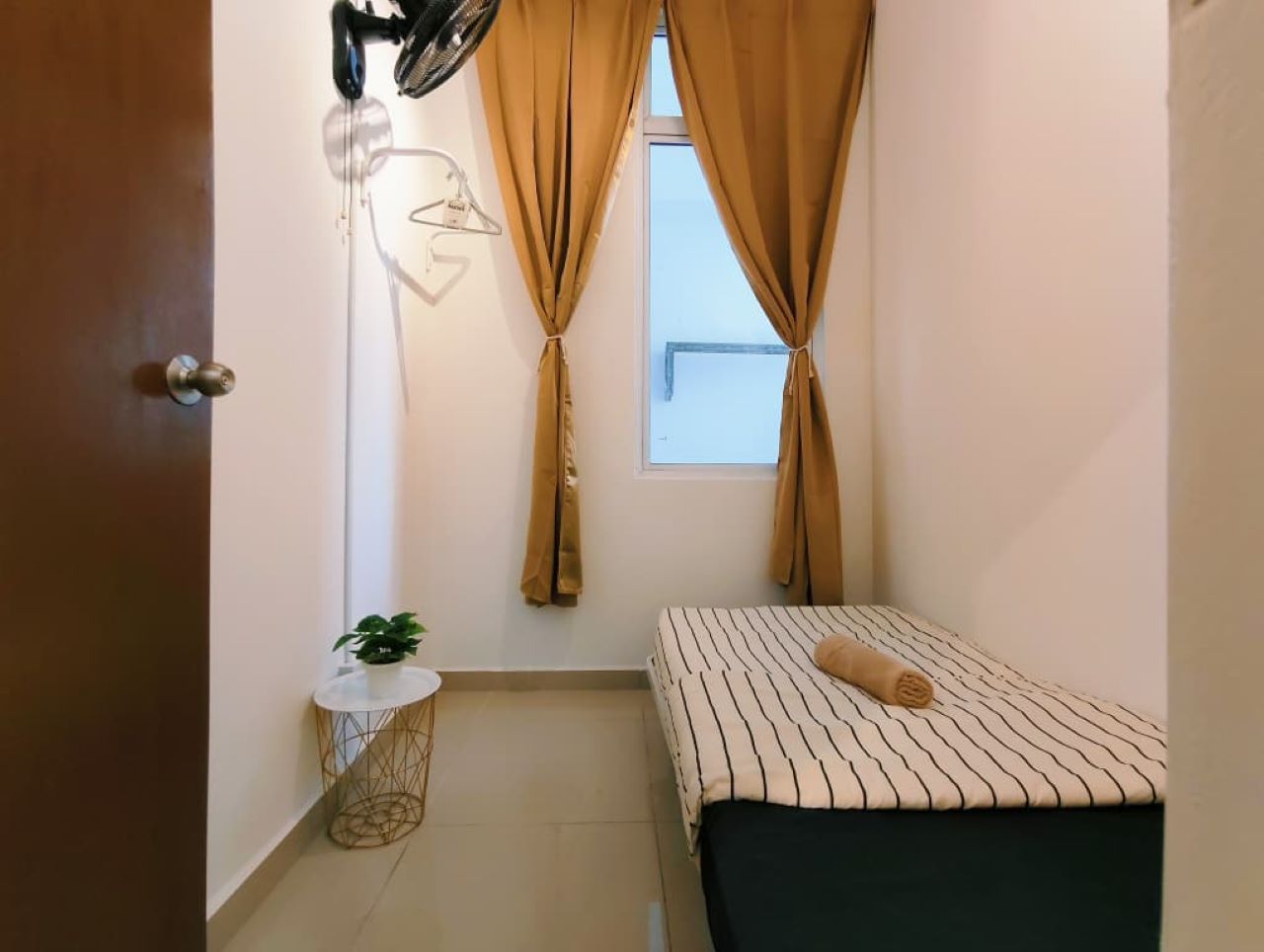 A small bedroom with a bed, a bedside table, a hanging light, and a window with curtains.