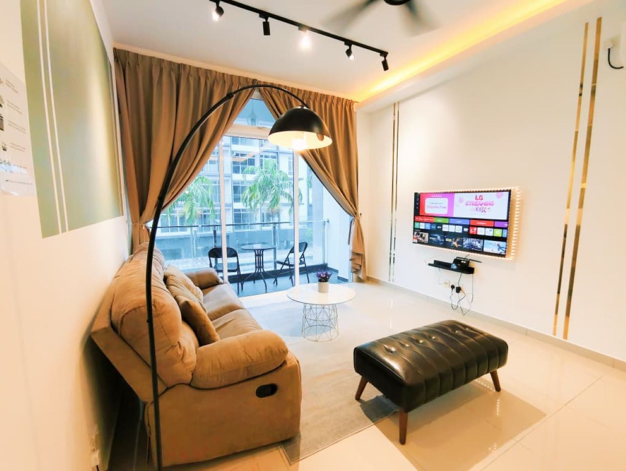A modern living room with a sofa, ottoman, and a flat-screen TV mounted on the wall.