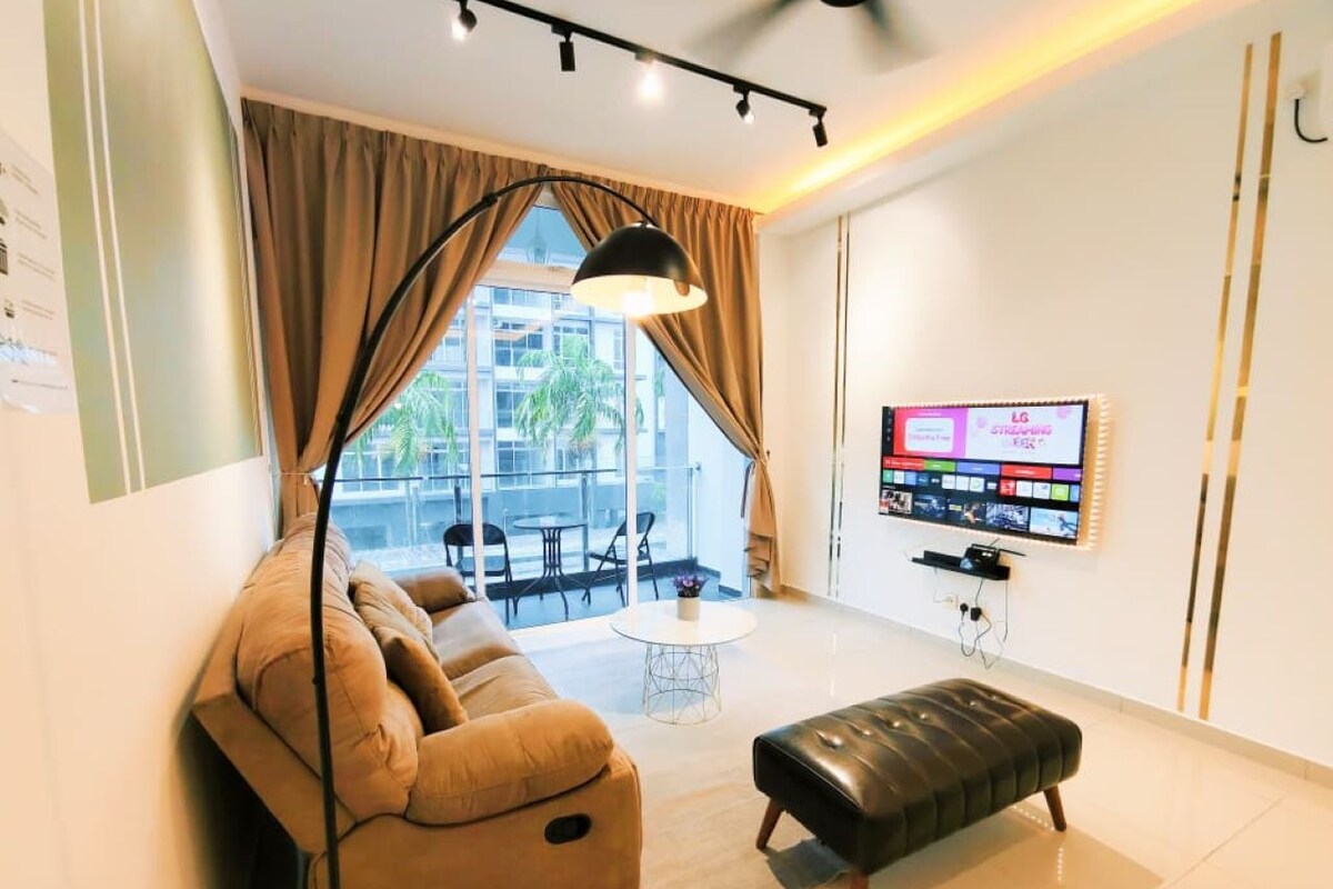 A modern living room with a sofa, ottoman, and a flat-screen TV mounted on the wall.