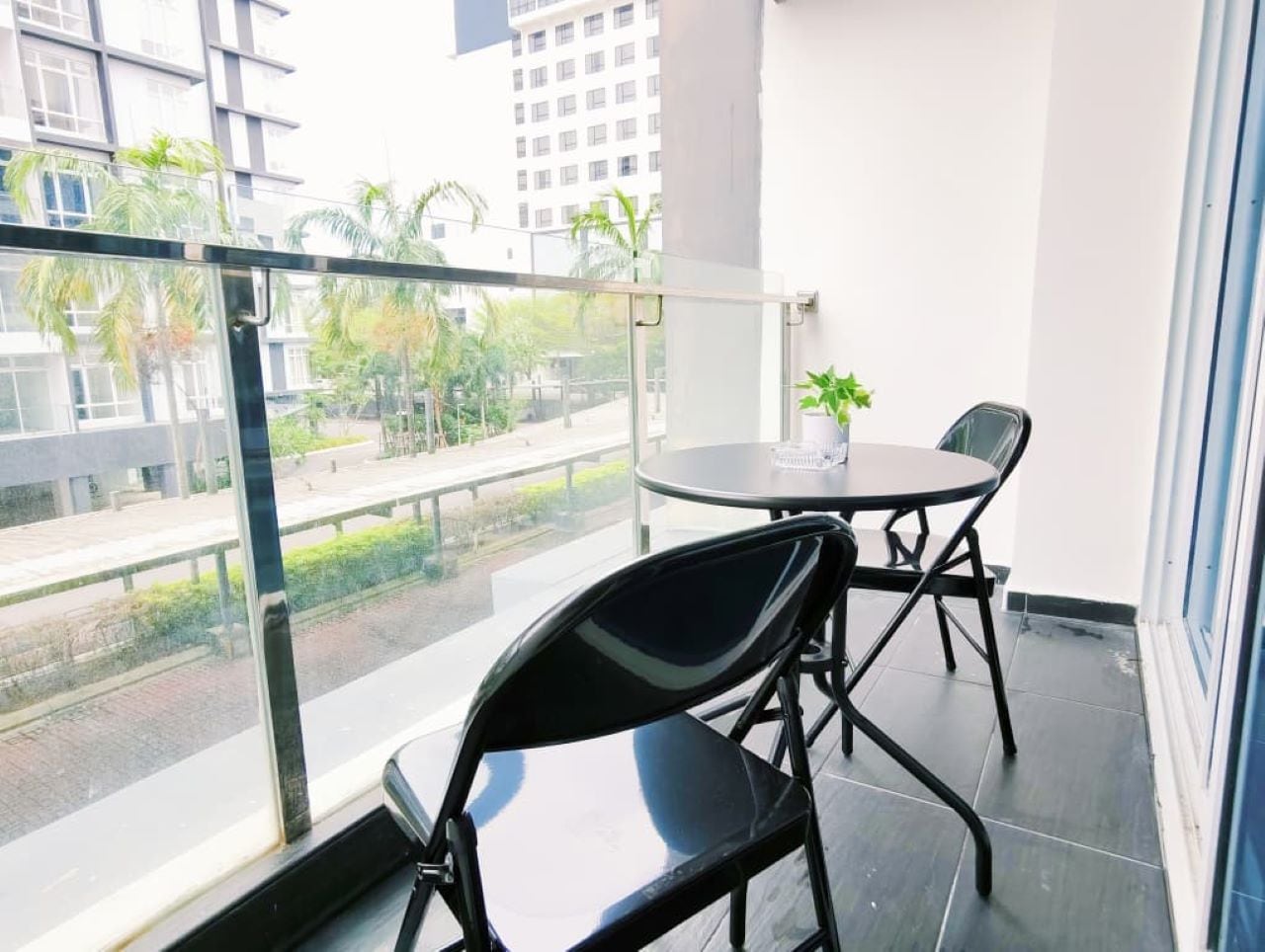 A balcony with a glass railing, two chairs, a small table, and a potted plant.