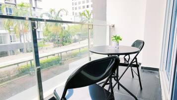 A balcony with a glass railing, two chairs, a small table, and a potted plant.