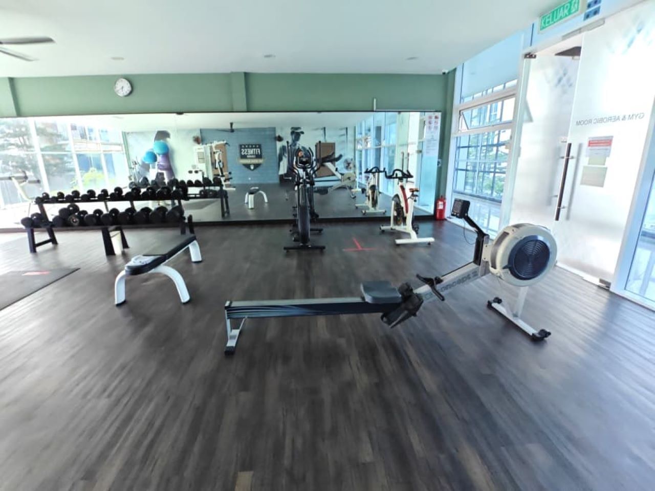 A gym with exercise equipment, a mirror, and a clock on the wall.