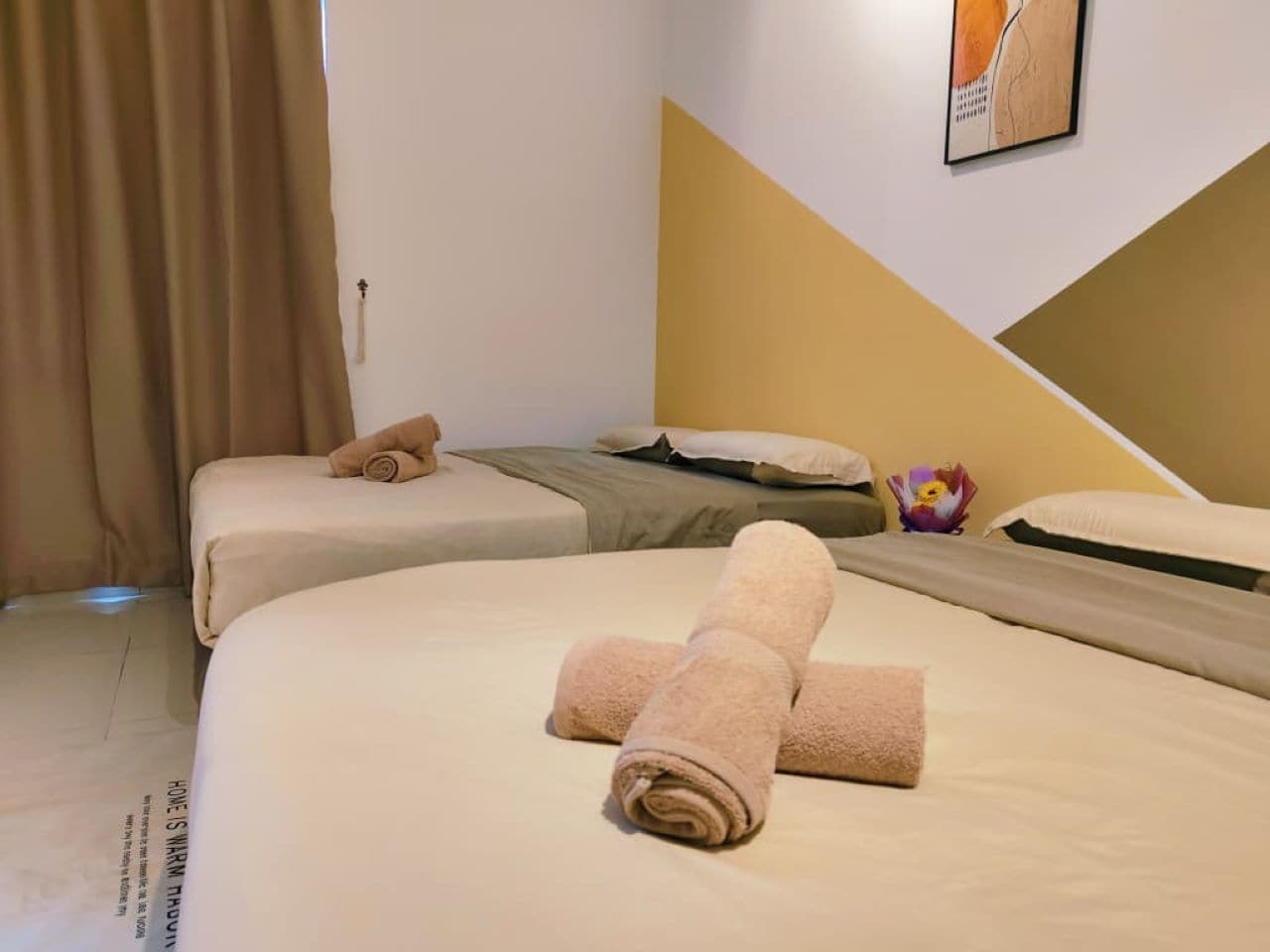 Une chambre d’hôtel avec deux lits, une literie de couleur beige, une œuvre d’art accrochée au mur et un lit avec une serviette roulée.