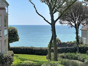 Ein Küstenblick mit blauem Himmel, einem von Bäumen gesäumten Weg und einem Gebäude mit Balkonen mit Blick aufs Meer.