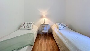 Un alojamiento pequeño, con una habitación individual, dos camas, una mesita de noche y una lámpara.