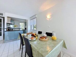 A dining area with a table set for breakfast, a kitchen in the background, and a view of the outdoors. - Le Vallon by Interhome (Pornic)
