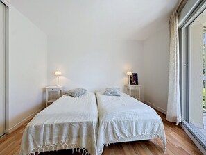 A room with two beds, white bedding, bedside lamps, a framed picture, and a window with curtains. - Le Vallon by Interhome (Pornic)