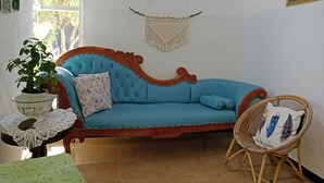 Una habitación con un sofá azul, una silla de mimbre, un tapiz de macramé y una planta en maceta.
