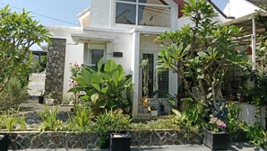 Una casa de dos pisos con fachada de piedra, un ventanal grande y varios maceteros con plantas en el jardín delantero.