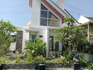 Una casa de dos pisos con fachada de piedra, un ventanal grande y varios maceteros con plantas en el jardín delantero.