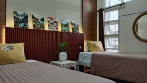 Habitación de hotel con dos camas, una mesita con una planta, una obra de arte en la pared y una ventana con persianas.
