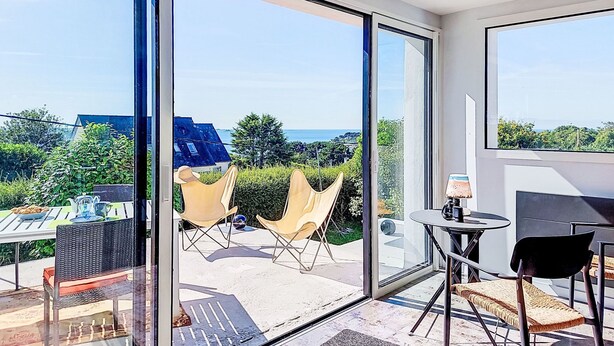 Une chambre moderne dotée de grandes portes vitrées donnant sur un espace extérieur avec vue sur la mer et la verdure.