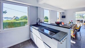 Une cuisine moderne dotée de grandes fenêtres, d’une cuisinière intégrée et d’un coin repas avec des chaises.