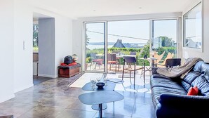 Un vaste espace de vie avec une grande porte-fenêtre coulissante donnant sur une terrasse extérieure, un canapé en cuir noir et une table à manger avec des chaises.