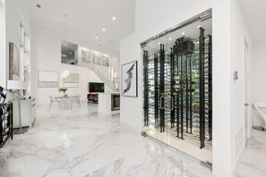 Un intérieur spacieux avec un cellier à vin en verre, un coin repas doté d’une table transparente et un escalier menant à un niveau supérieur.
