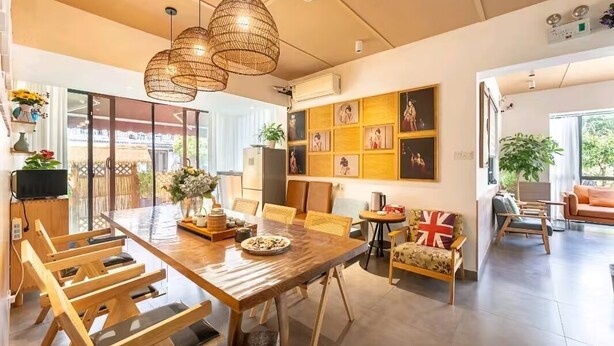 A modern dining area with a wooden table, wicker pendant lights, and a wall with framed pictures.