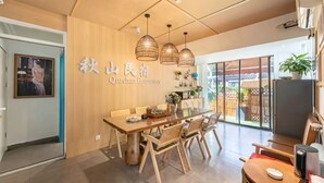 A modern interior with a wooden dining table, chairs, pendant lights, and a visible sign reading 'Qishan Homestay'.
